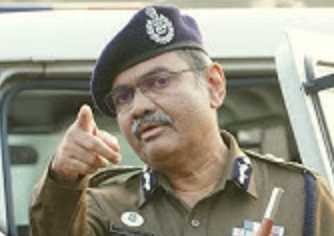 Narasimha Komar in uniform and beret gesturing while giving directions outdoors beside a police vehicle.