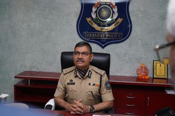 Narasimha Komar seated at his desk in Gujarat Police uniform beneath the Gujarat Police emblem.