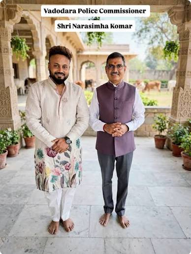Narasimha Komar standing in a maroon waistcoat beside a visitor in a heritage courtyard, under a banner reading Vadodara Police Commissioner Shri Narasimha Komar.