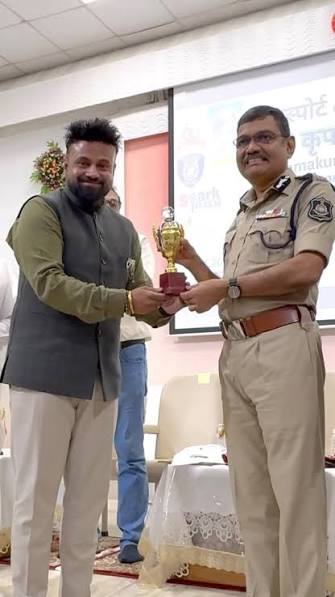 Narasimha Komar in uniform receiving a small trophy from a guest at an indoor function.