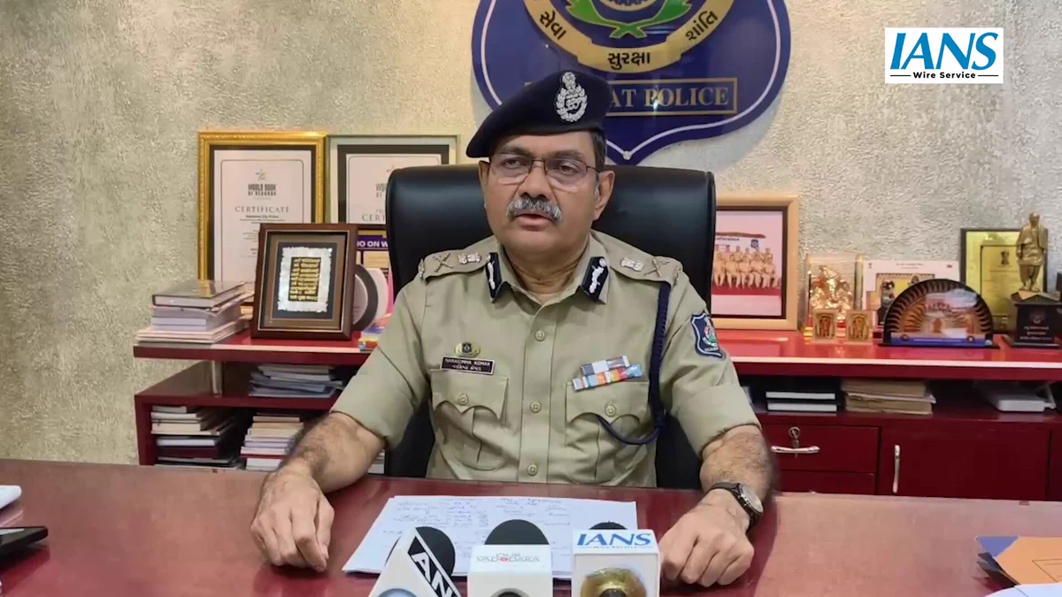 Narasimha Komar in Gujarat Police uniform at his desk, addressing a press briefing beneath the Gujarat Police emblem.