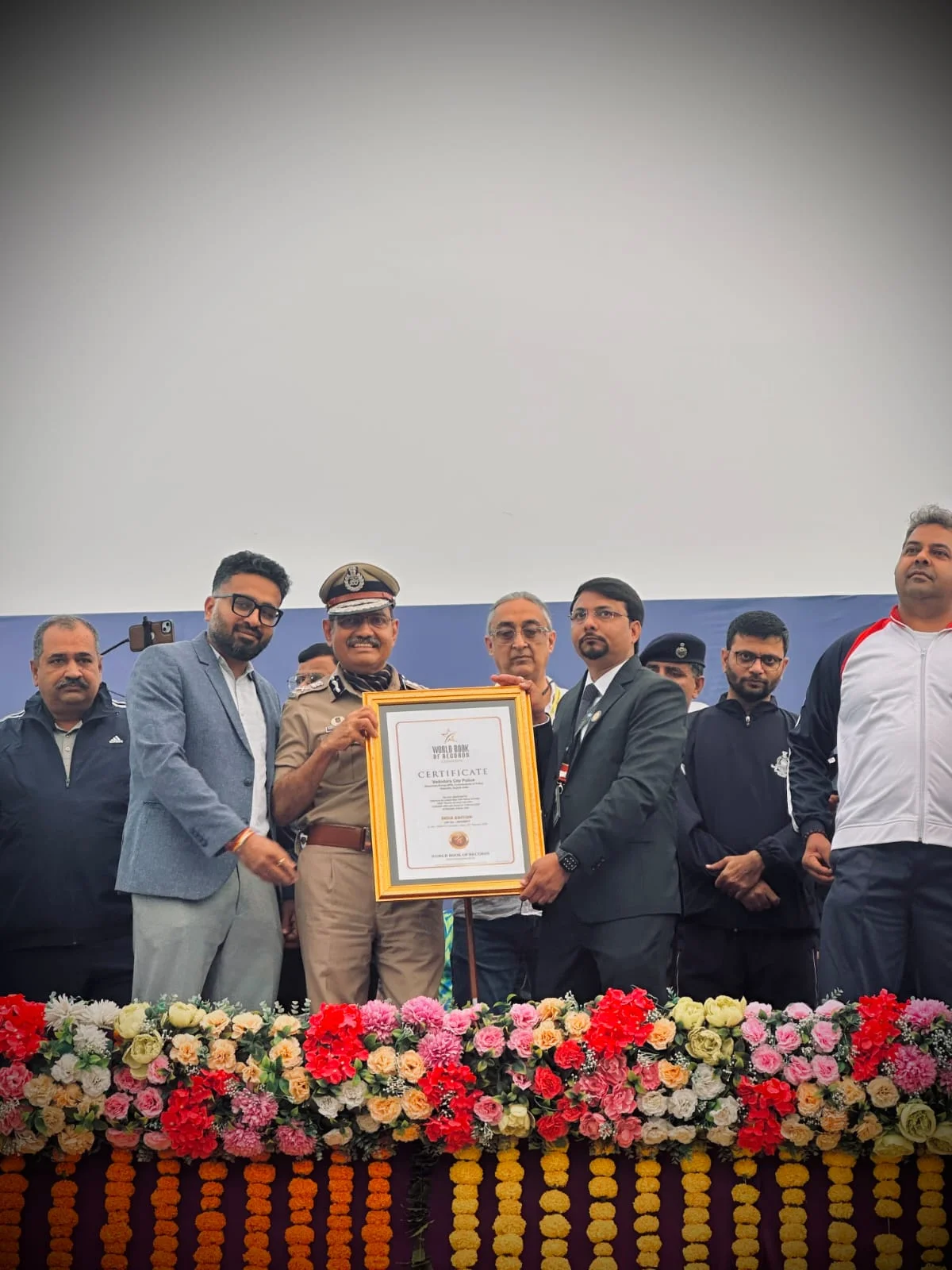 Narasimha Komar in ceremonial uniform holding the framed World Book of Records certificate on stage with officials and organisers.