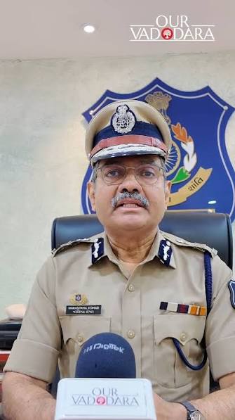Narasimha Komar in peaked cap and uniform speaking to reporters from behind his desk in Vadodara.