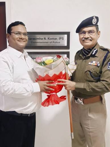 Narasimha Komar in uniform receiving a bouquet beside the office nameplate reading Narasimha N. Komar, IPS, Commissioner of Police.