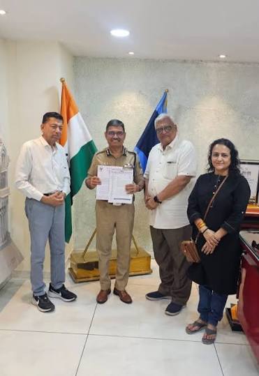 Narasimha Komar in uniform holding a document alongside three visitors in his office, beside the national flag.